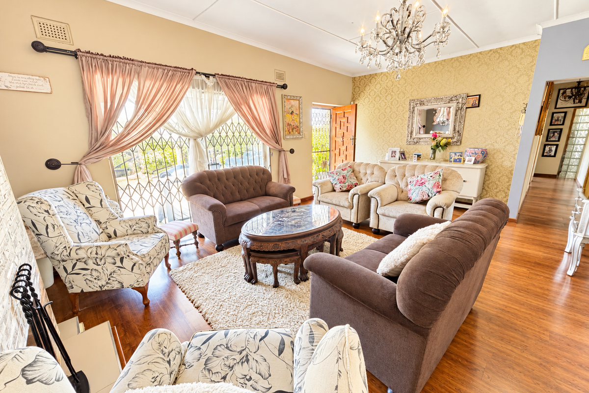 A spacious living room featuring laminate flooring, a decorative crystal chandelier, and a fireplace, offering a warm and inviting atmosphere.