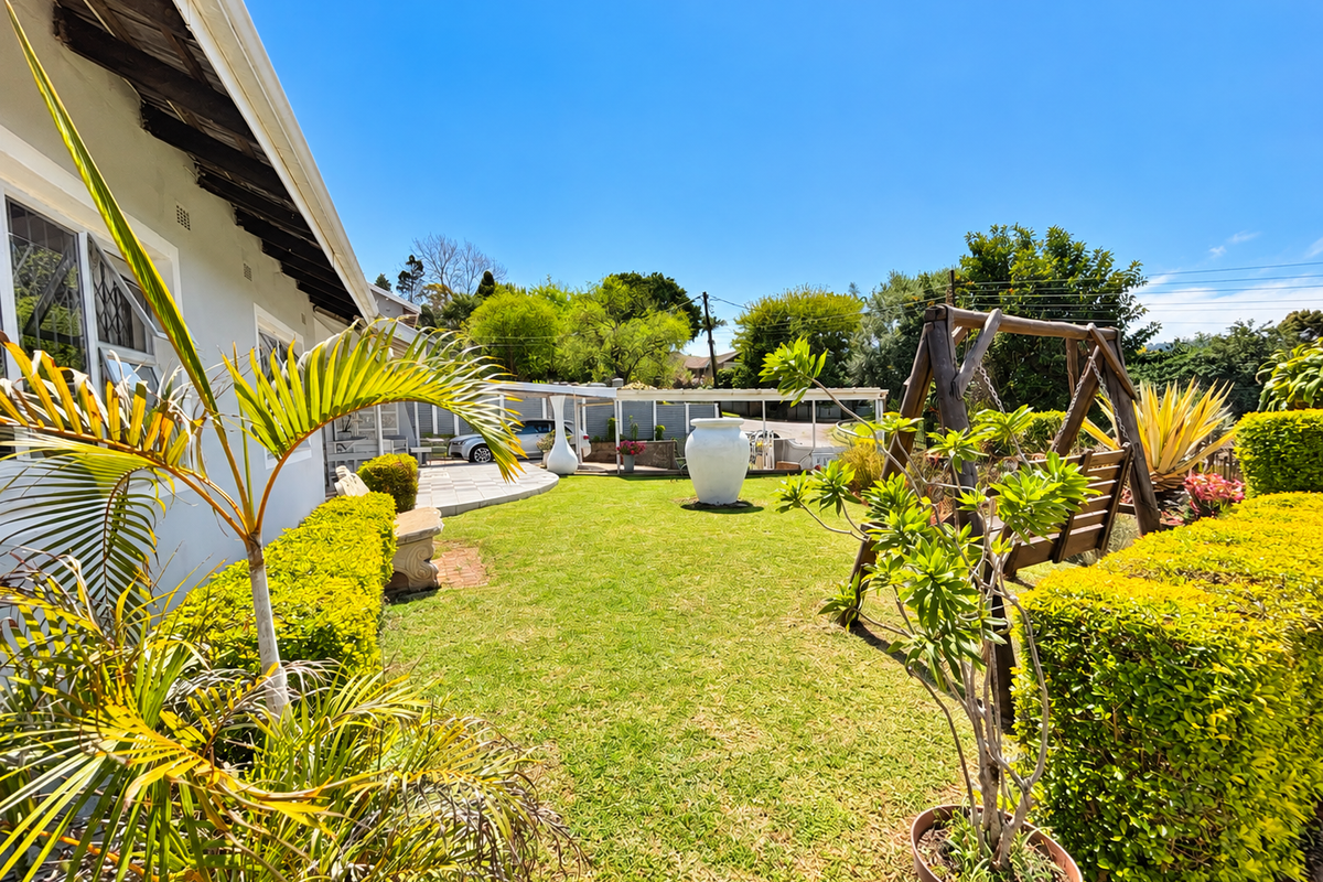 A well-maintained rear garden featuring a manicured lawn, established hedges, and a paved patio area with a covered pergola structure.