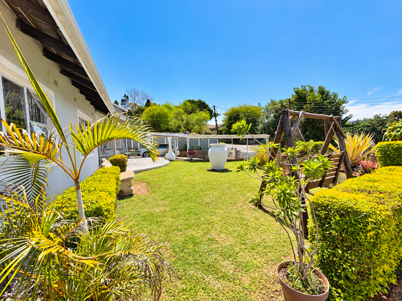A well-maintained rear garden featuring a manicured lawn, established hedges, and a paved patio area with a covered pergola structure.