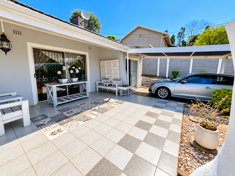 A well-maintained covered patio area featuring decorative tiled flooring, sliding glass doors, and an adjacent carport for vehicle parking.