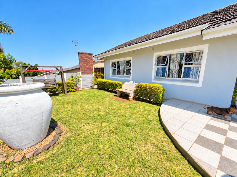 A well-maintained rear garden featuring a tiled patio area, manicured lawn, and secure windows with fitted security bars.