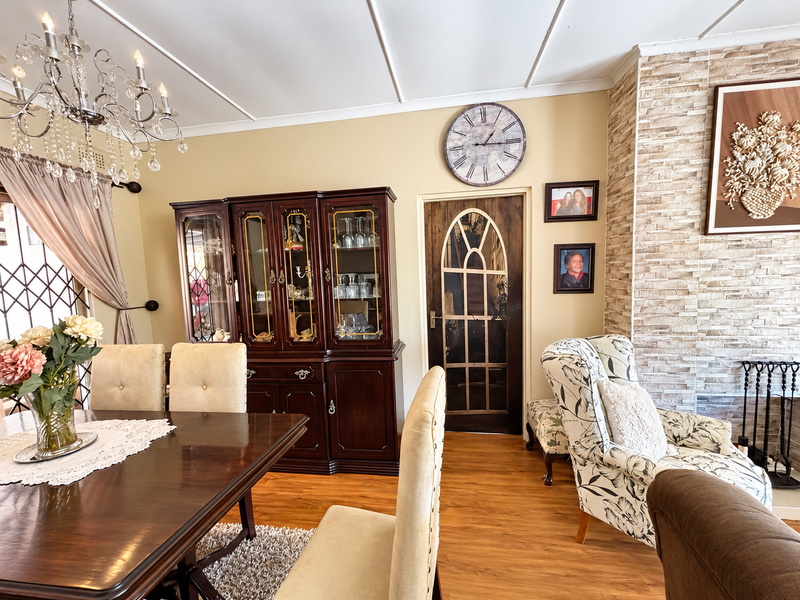 A dining area featuring laminate flooring, a stone-clad fireplace feature wall, and a decorative glass-panelled door, offering a traditional aesthetic.