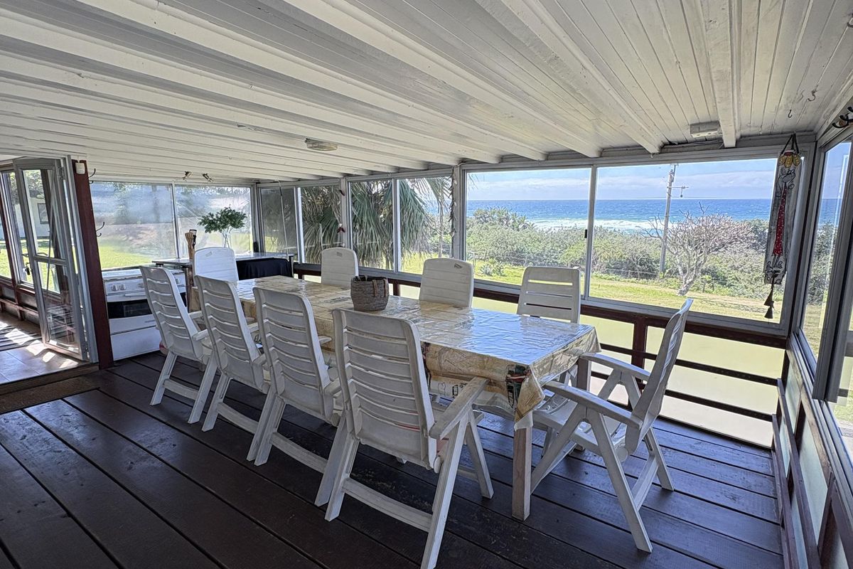 Spacious covered patio featuring timber decking and expansive sliding glass windows with direct ocean views, perfect for outdoor dining and relaxation.