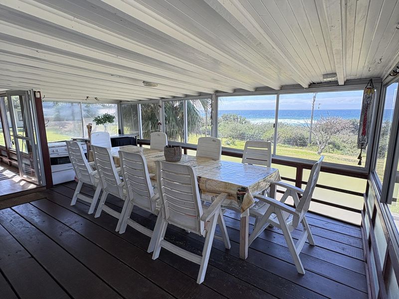Spacious covered patio featuring timber decking and expansive sliding glass windows with direct ocean views, perfect for outdoor dining and relaxation.