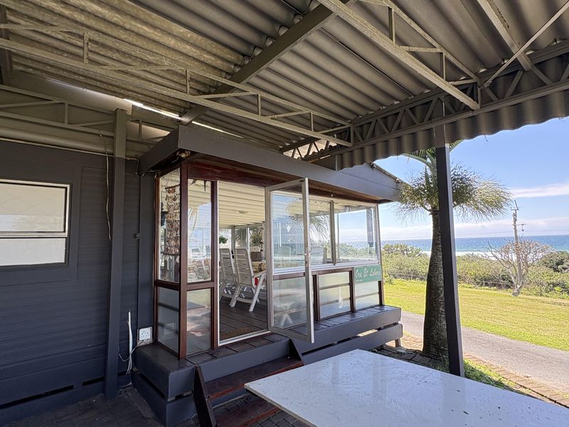 Covered outdoor patio area featuring a paved floor, corrugated metal roof, and an enclosed timber-framed structure with direct access to the garden and ocean views.