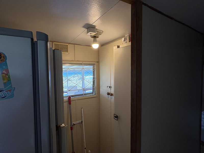 A compact utility space featuring built-in storage cabinetry, a small window with security grille, and basic overhead lighting.