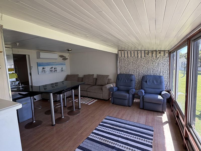 Open plan living area featuring laminate flooring, timber panelled ceiling, split system air conditioning, and a breakfast bar with large windows overlooking the garden.