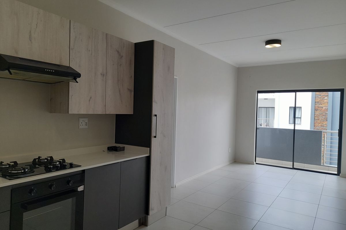 Modern open-plan kitchen and living area featuring sleek cabinetry, built-in appliances, tiled flooring, and direct access to a private balcony.