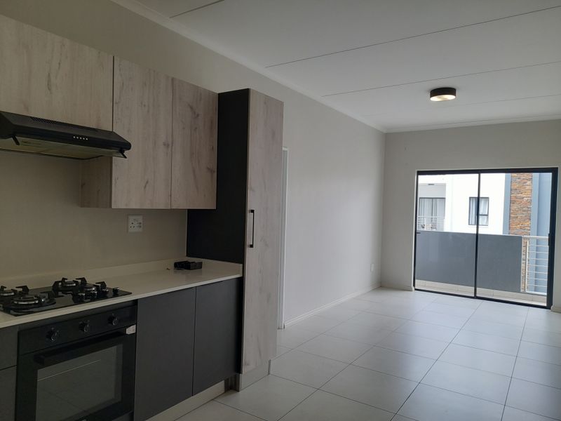 Modern open-plan kitchen and living area featuring sleek cabinetry, built-in appliances, tiled flooring, and direct access to a private balcony.