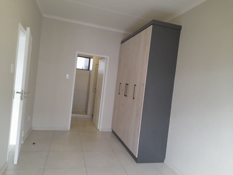 A clean, neutral bedroom featuring modern built-in wardrobes, tiled flooring, and direct access to an en-suite bathroom.