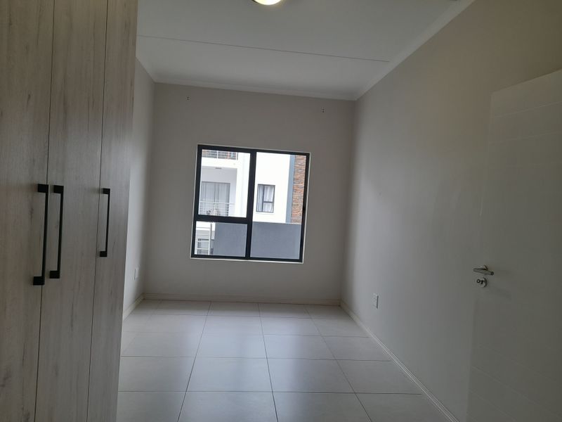 A clean, empty bedroom featuring neutral tiled flooring and modern built-in cupboards, offering a blank canvas for personalization.