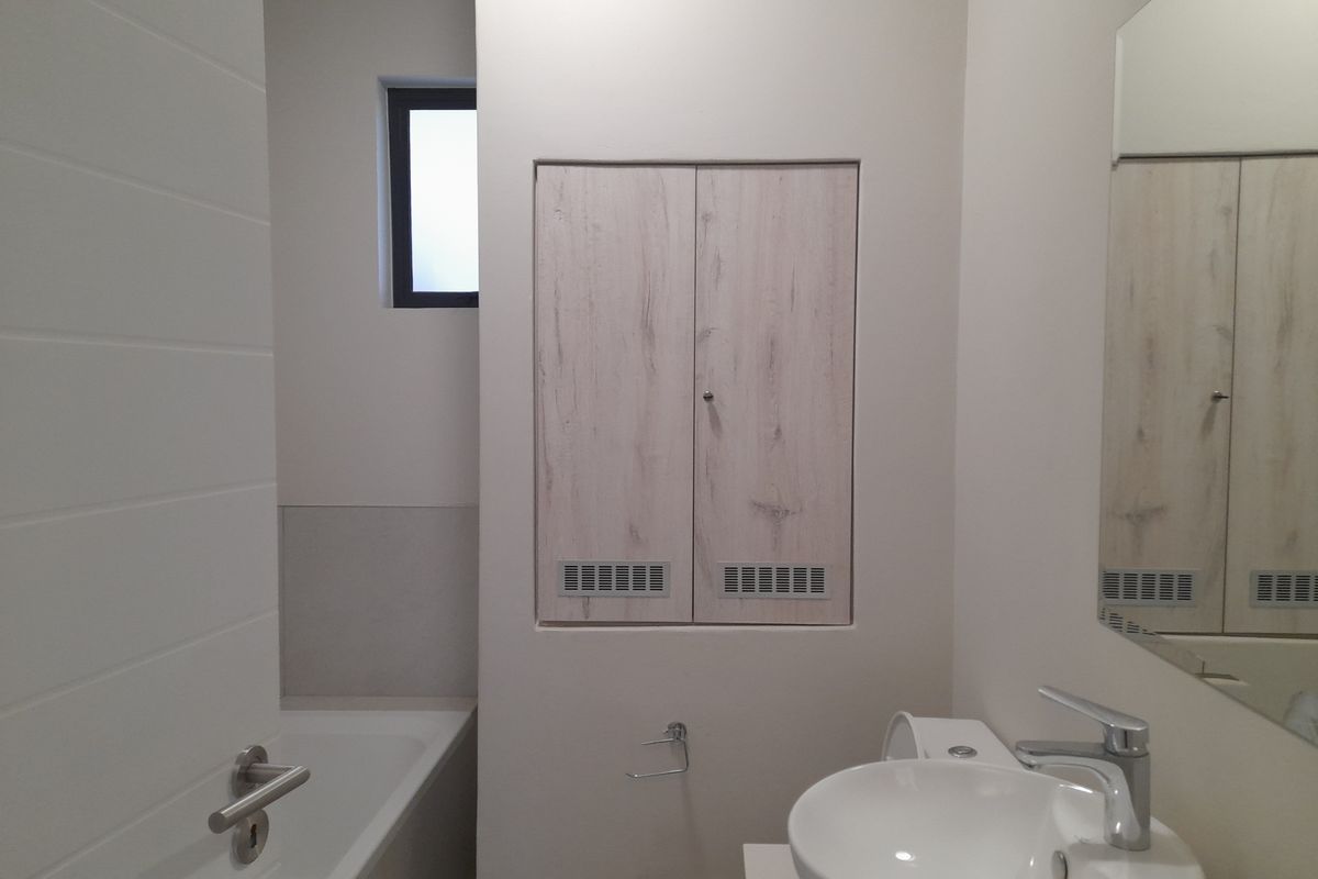 A clean, modern bathroom featuring a built-in vanity, white basin with mixer tap, bathtub, and wall-mounted mirror in a neutral, well-maintained space.