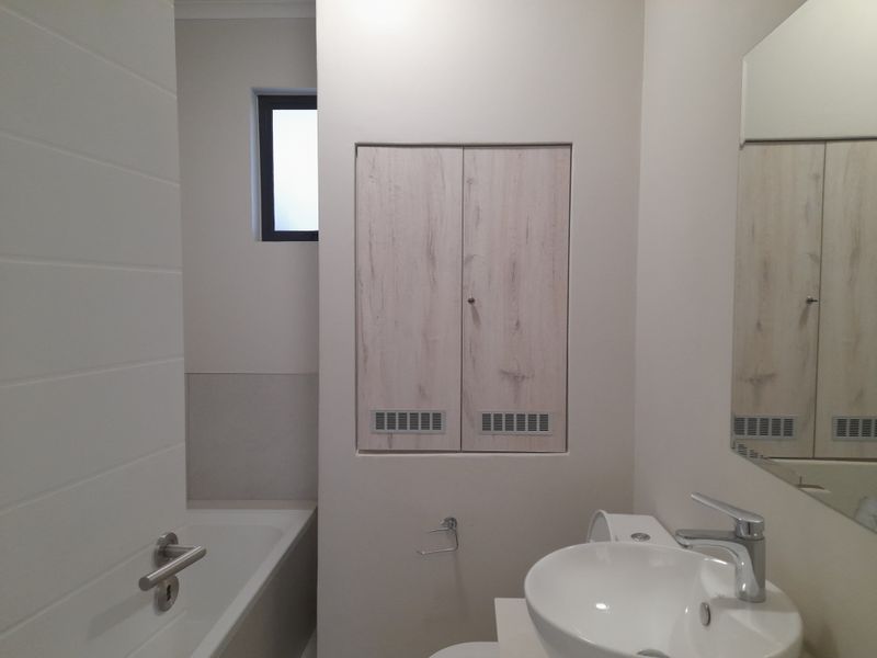 A clean, modern bathroom featuring a built-in vanity, white basin with mixer tap, bathtub, and wall-mounted mirror in a neutral, well-maintained space.