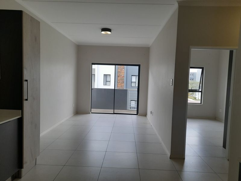 A bright and spacious open-plan living area featuring neutral tiled flooring, modern ceiling lighting, and a large sliding glass door leading to an outdoor space.