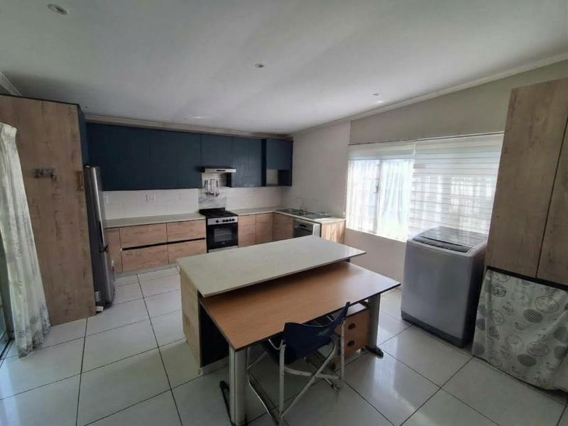 Modern kitchen featuring two-tone cabinetry, stone countertops, built-in oven and hob, extractor fan, and tiled flooring with ample natural light.