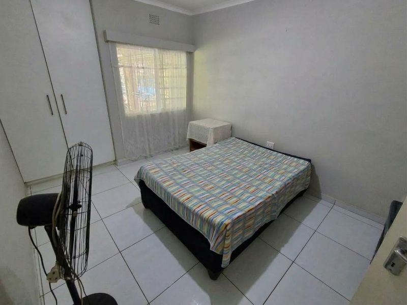 A functional bedroom featuring tiled flooring, a built-in wardrobe, and a window with security bars, offering a clean and simple living space.