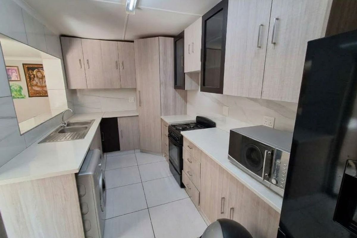 A functional kitchen featuring light wood-tone cabinetry, stone-look countertops, tiled flooring, and integrated space for laundry appliances.