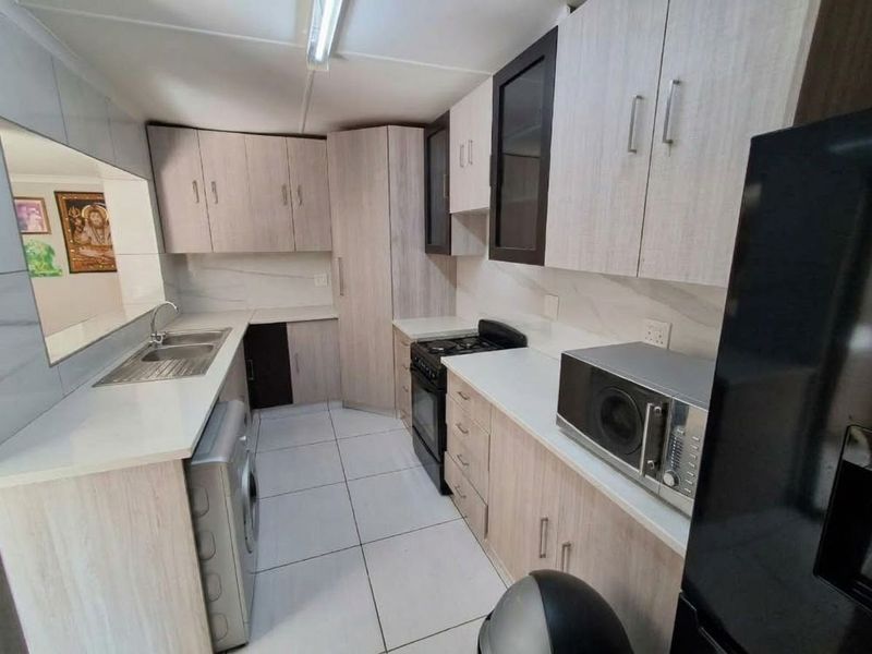 A functional kitchen featuring light wood-tone cabinetry, stone-look countertops, tiled flooring, and integrated space for laundry appliances.