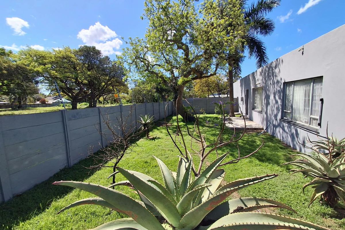 A rear garden featuring a lawn, mature trees, and a precast concrete boundary wall, adjacent to the house with aluminium window frames.