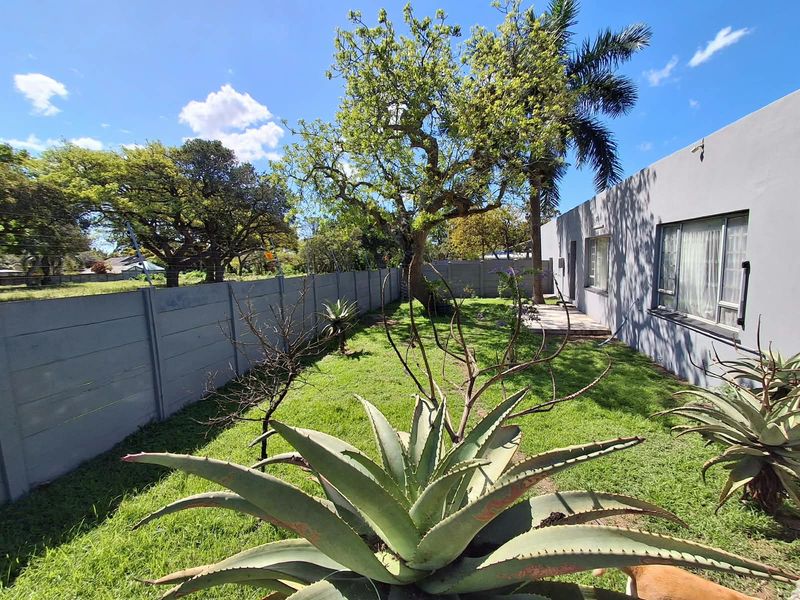 A rear garden featuring a lawn, mature trees, and a precast concrete boundary wall, adjacent to the house with aluminium window frames.