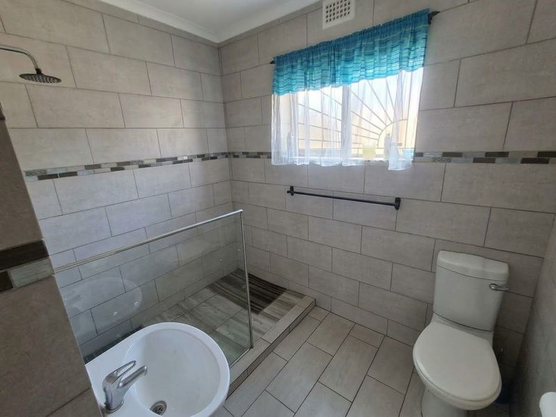 A modern bathroom featuring a walk-in shower with a glass screen, neutral ceramic tiling, and a standard toilet.