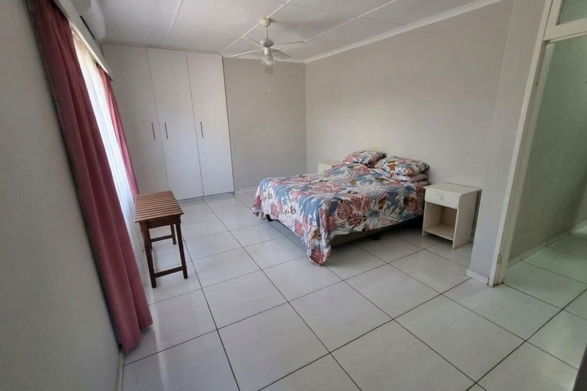 Spacious bedroom featuring tiled flooring, built-in cupboards, a ceiling fan, and an integrated air conditioning unit.