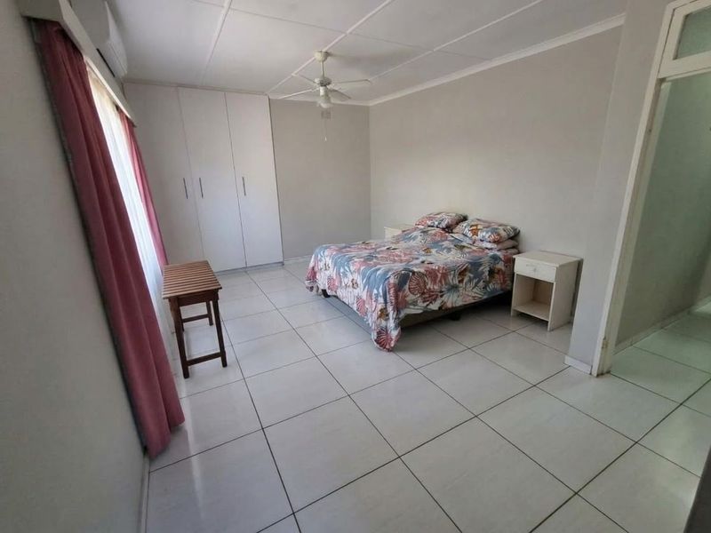 Spacious bedroom featuring tiled flooring, built-in cupboards, a ceiling fan, and an integrated air conditioning unit.