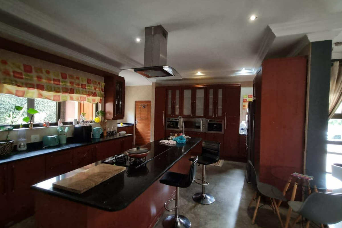 Spacious kitchen featuring dark wood cabinetry, granite countertops, a central island with a built-in cooktop, and modern stainless steel extractor fan.
