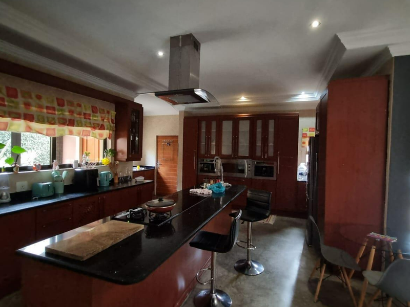 Spacious kitchen featuring dark wood cabinetry, granite countertops, a central island with a built-in cooktop, and modern stainless steel extractor fan.