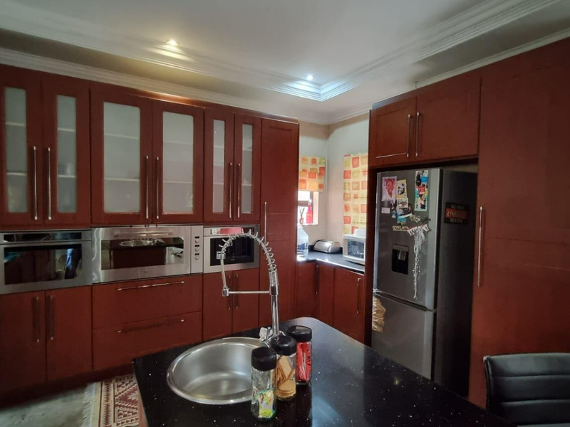 A well-appointed kitchen featuring dark wood cabinetry, granite countertops, a central island with a sink, and integrated built-in appliances.