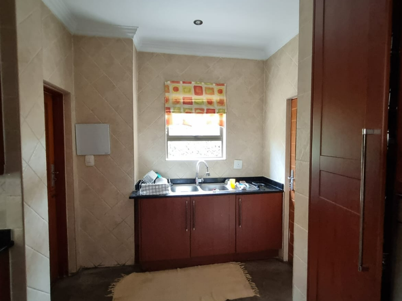 A functional scullery area featuring dark wood cabinetry, granite countertops, a double sink, and tiled wall finishes.
