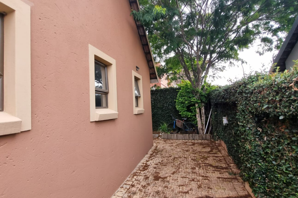 A side exterior view of the property featuring a paved walkway, plastered walls with casement windows, and a mature ivy-covered boundary wall.
