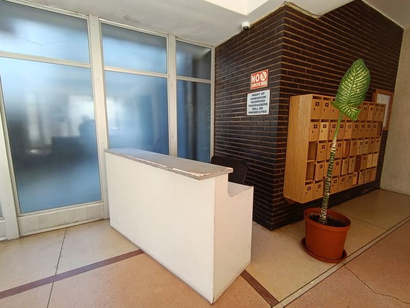Building entrance lobby featuring a reception desk, wall-mounted mailboxes, and a brick feature wall with terrazzo flooring.