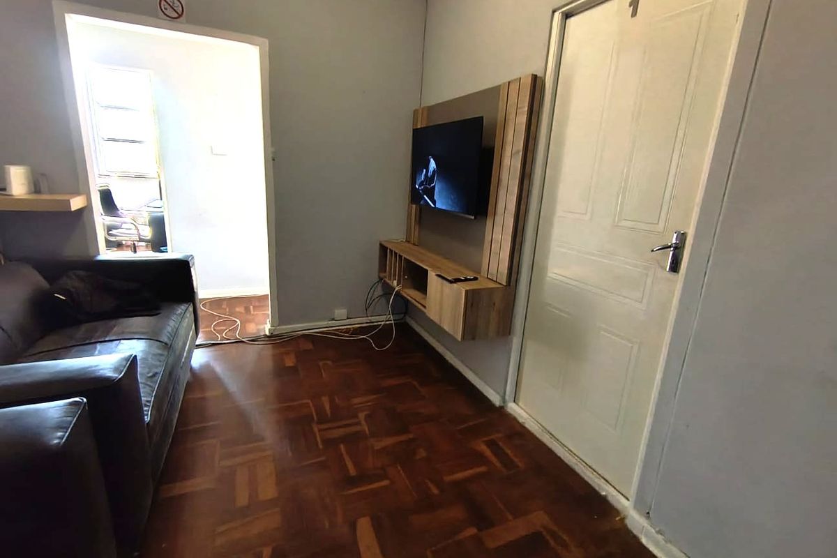 A living room featuring parquet flooring and a built-in media console, with an adjacent doorway leading to another room.
