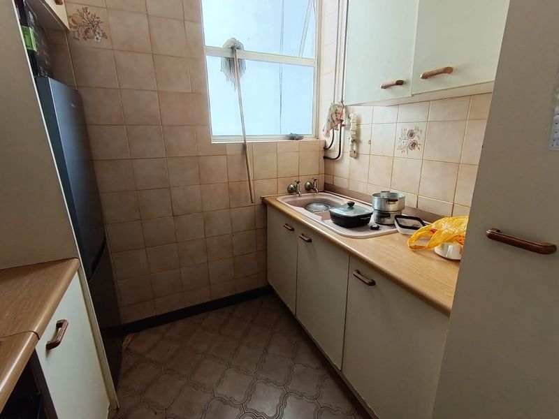 A compact, dated kitchen featuring original cabinetry, laminate countertops, and tiled splashbacks, offering potential for a modern renovation.