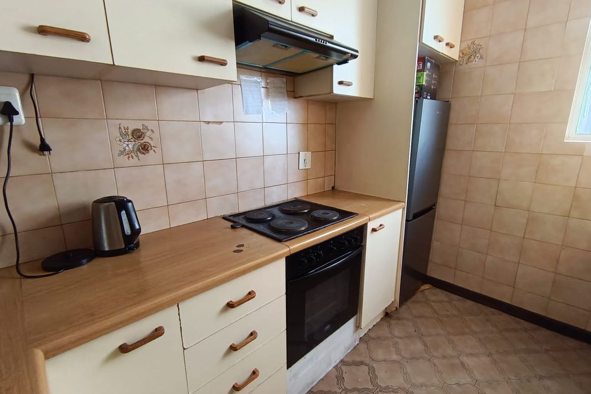 A functional kitchen featuring dated cabinetry, laminate countertops, an integrated electric hob and oven, and tiled wall finishes.