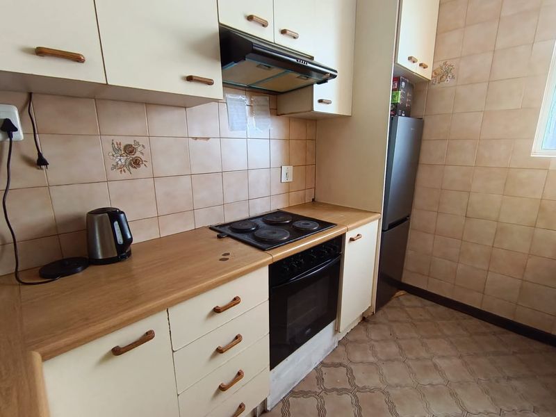 A functional kitchen featuring dated cabinetry, laminate countertops, an integrated electric hob and oven, and tiled wall finishes.