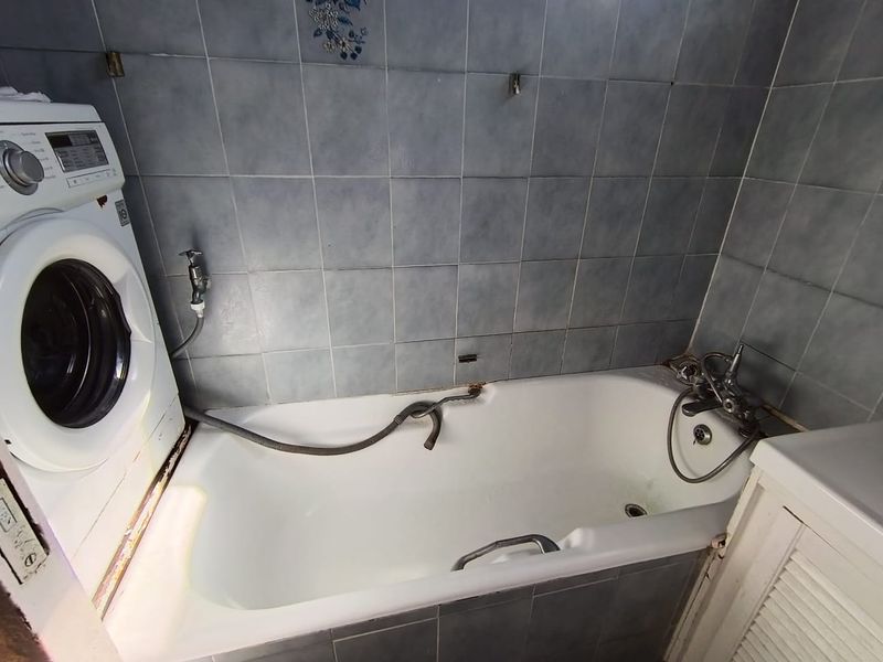 A functional bathroom featuring a bathtub with integrated shower mixer and tiled wall finishes, currently accommodating a laundry appliance.