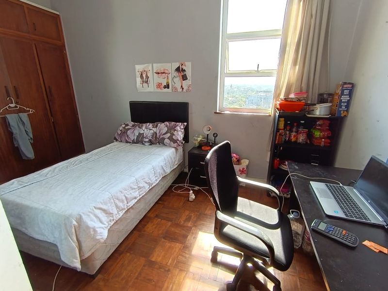 A bedroom featuring parquet flooring, a built-in wooden wardrobe, and a large window providing natural light and an elevated view.