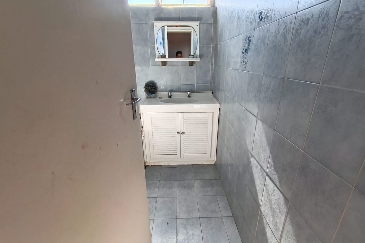 A compact bathroom featuring a vanity cabinet with basin, wall mirror, and full-height wall tiling. The space is ready for a modern renovation.