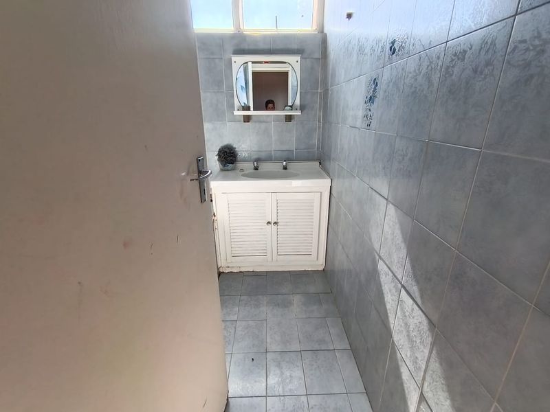 A compact bathroom featuring a vanity cabinet with basin, wall mirror, and full-height wall tiling. The space is ready for a modern renovation.