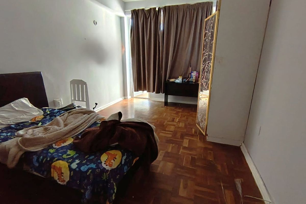 A bedroom featuring parquet flooring and a sliding glass door leading to an outdoor area, offering potential for cosmetic updates.