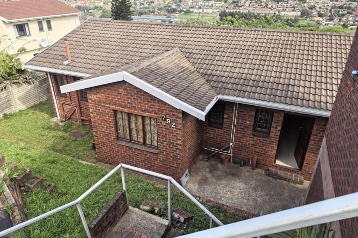 Elevated view of the rear exterior featuring a facebrick facade, concrete tile roof, and a paved patio area overlooking the surrounding neighborhood.