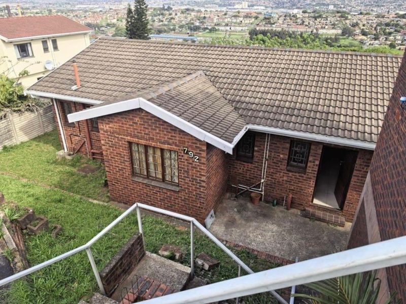 Elevated view of the rear exterior featuring a facebrick facade, concrete tile roof, and a paved patio area overlooking the surrounding neighborhood.