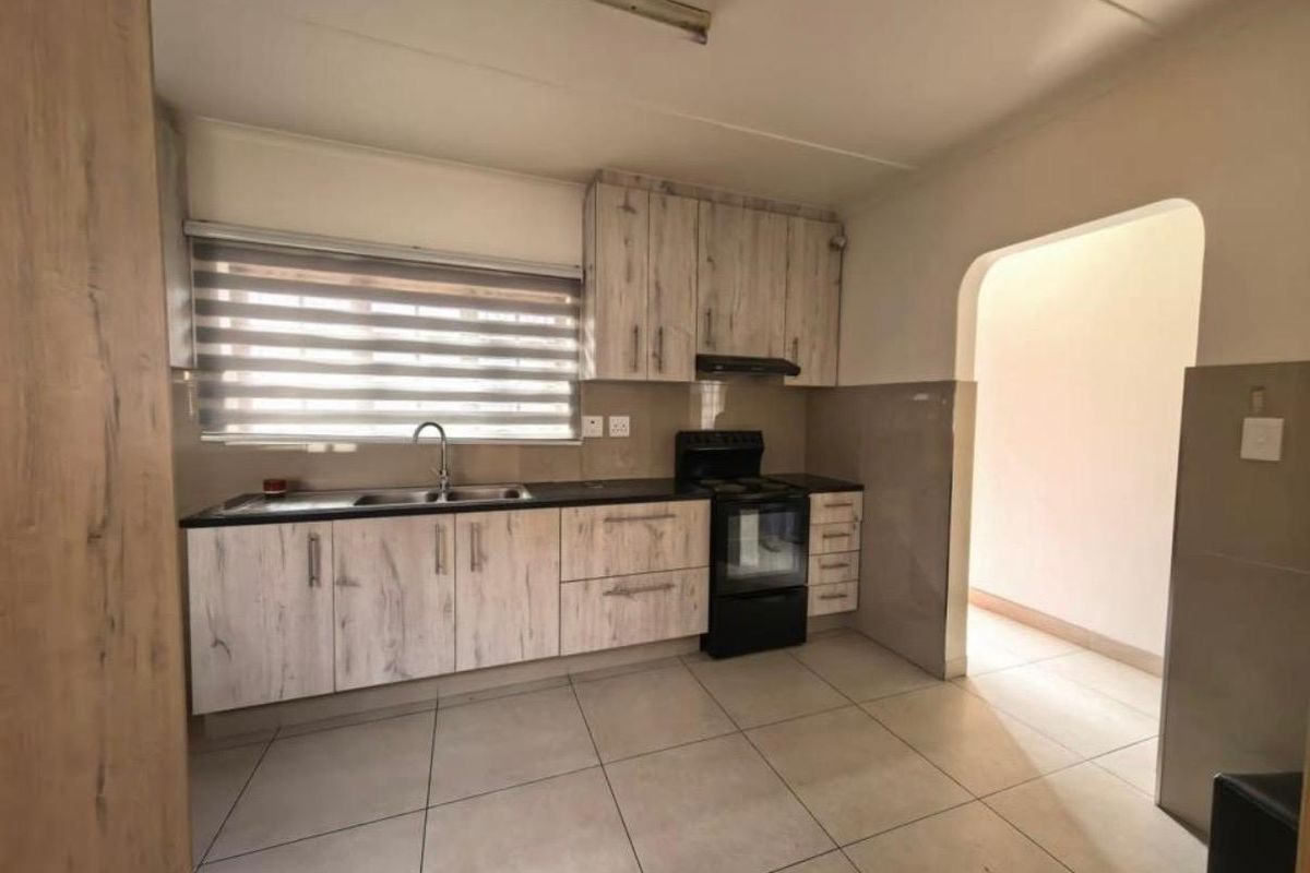 A clean and functional kitchen featuring light wood-grain cabinetry, tiled flooring, and a built-in extractor fan with a double sink.