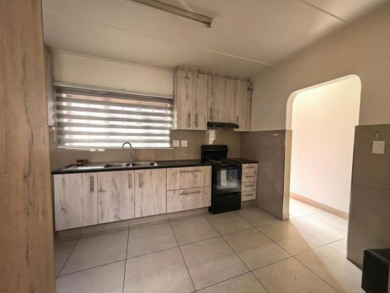 A clean and functional kitchen featuring light wood-grain cabinetry, tiled flooring, and a built-in extractor fan with a double sink.