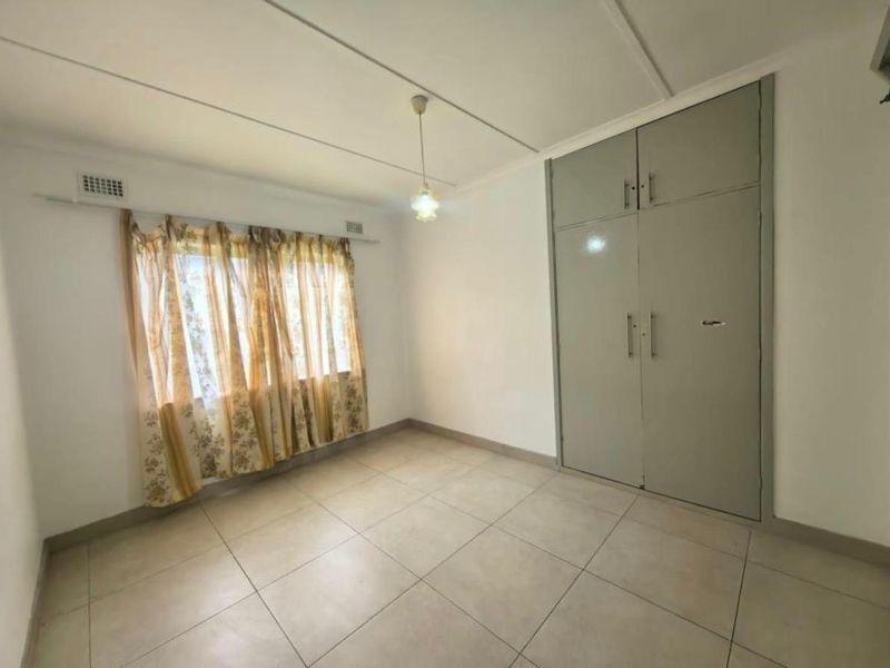 A clean, empty bedroom featuring neutral tiled flooring and built-in cupboards, offering a blank canvas for personalization.