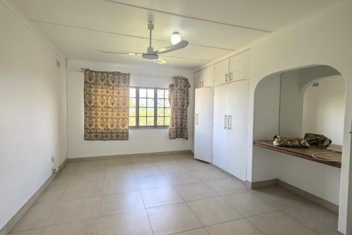 Spacious bedroom featuring neutral tiled flooring, built-in cupboards, a ceiling fan, and a built-in vanity area.