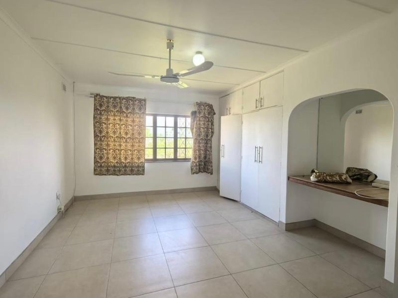 Spacious bedroom featuring neutral tiled flooring, built-in cupboards, a ceiling fan, and a built-in vanity area.