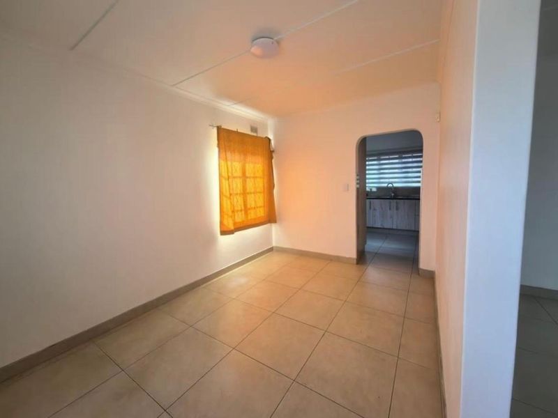 A bright, empty living area featuring neutral tiled flooring and an arched doorway leading to the kitchen.
